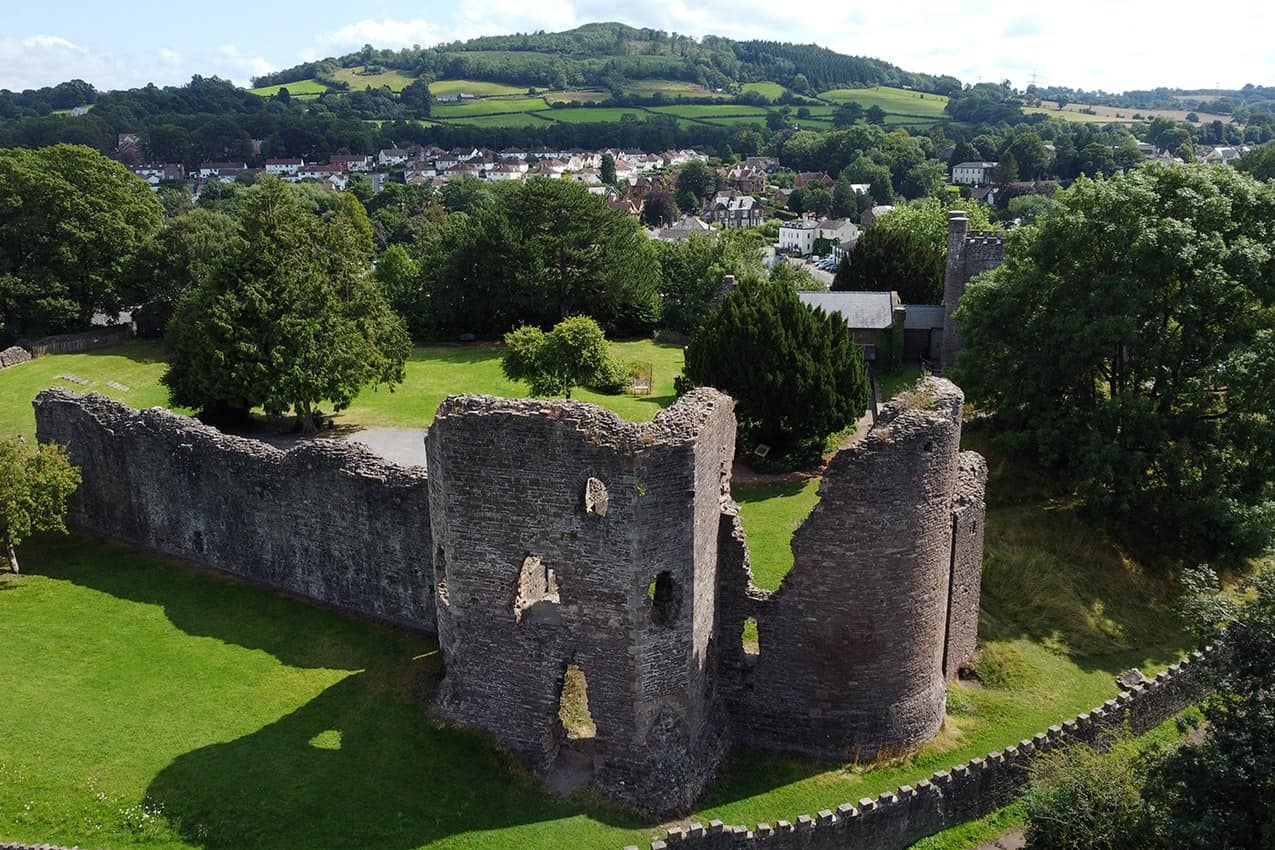 An aerial drone photograph of Abergavenny Castle, against the backdrop of lush green Welsh hills.