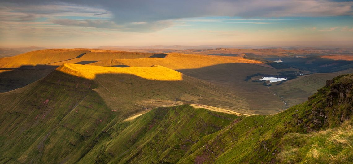 A sunlight view of the Cribyn mountain peaks and Upper Neuadd reservoir from Pen Y Fan, in the Bannau Brycheiniog National Park, Wales.