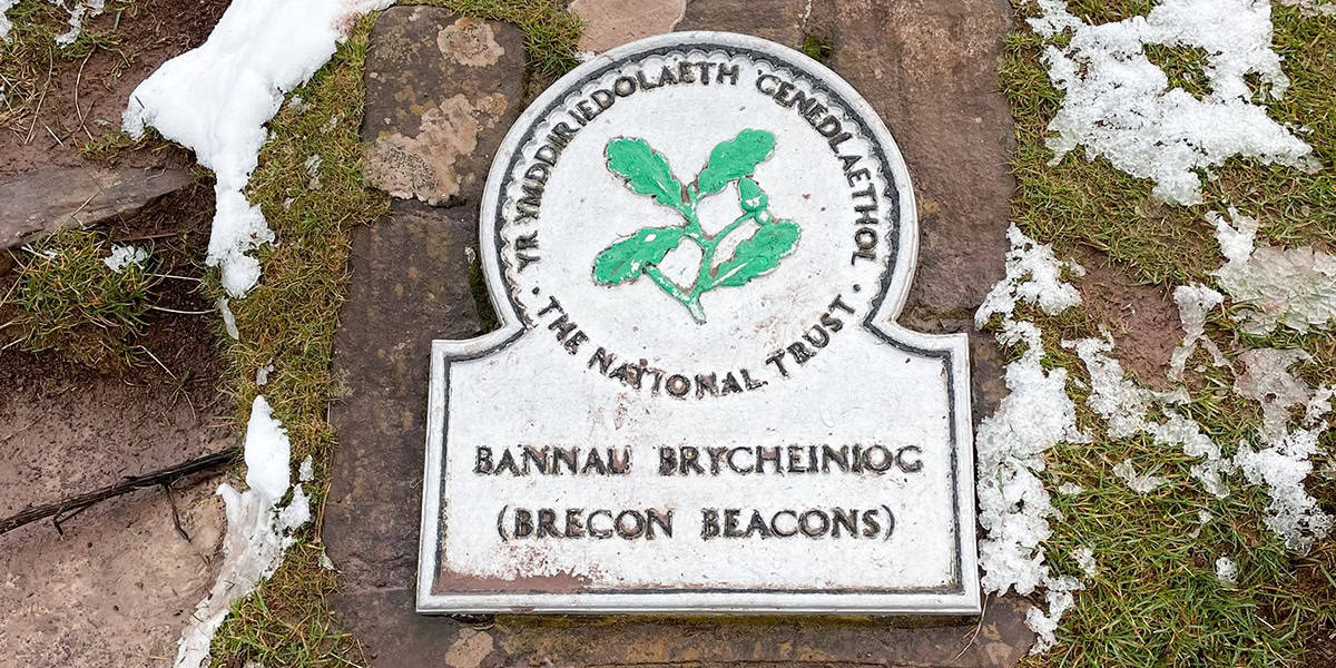 A National Trust plaque set in stone on a partially snow covered ground on Pen Y Fan, Bannau Brycheiniog.